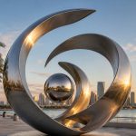 Orbital Flow contemporary stainless steel abstract sculpture by FORMA Sculptures, featuring flowing orbital forms and a reflective sphere for landmark waterfront public art and luxury developments.